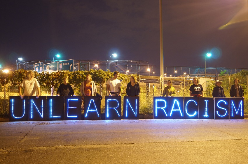 Members of the Overpass Light Brigade holding lighted signs spelling out "Unlearn Racism" (Creative Commons / flickr user Joe Brusky)