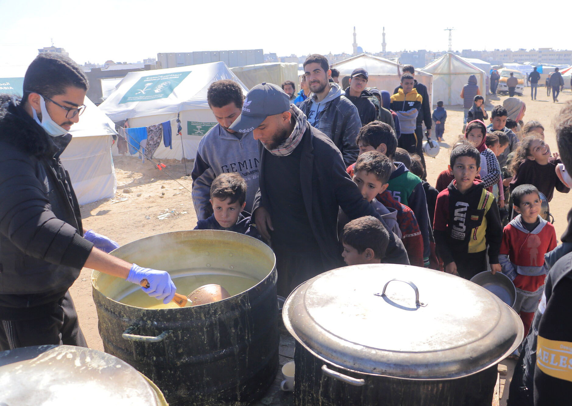 Volunteer spoons food out of a large pot as a crowd of children stand beside