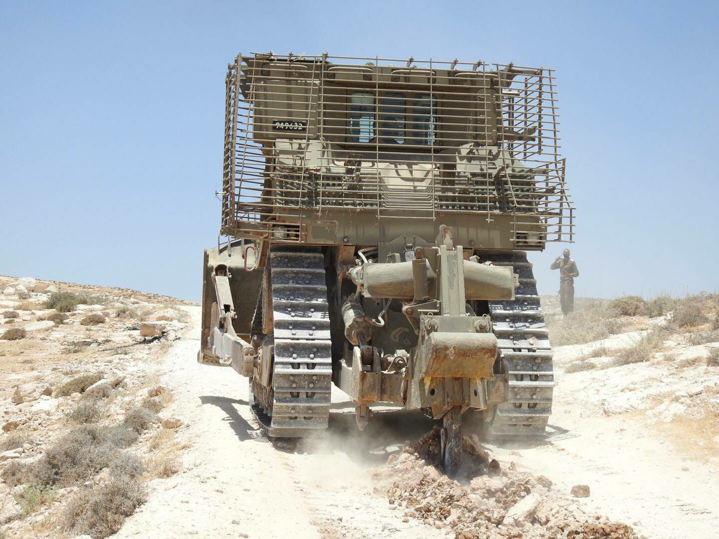 An earth moving vehicle demolishing a road as part of a forced displacement in the West Bank