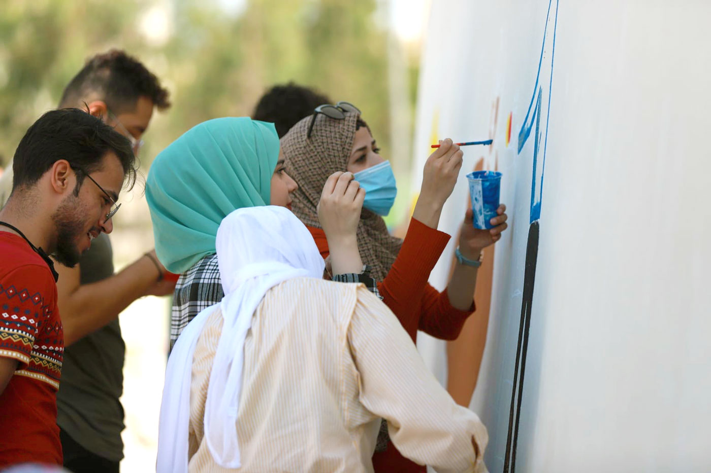 Young Jordanians painting a mural together on a wall