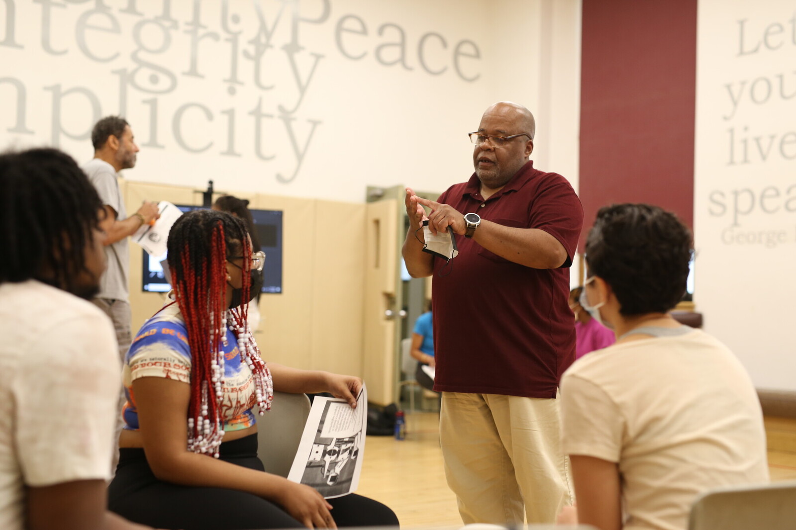 person standing in gymnasium talking to a group of youth