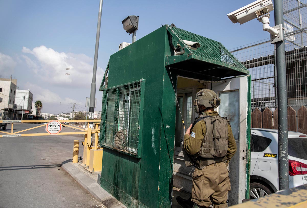An Israeli soldier checks cars at a checkpoint on a city street