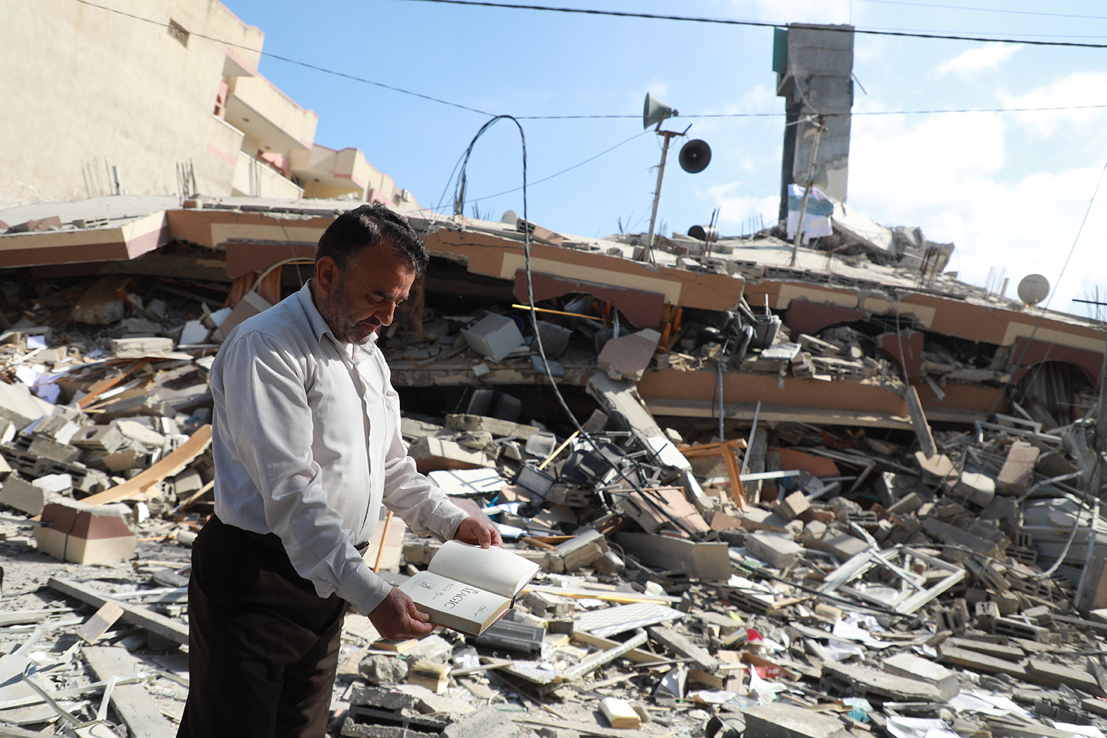 man opening up a book standing in front of a pile of rubble 