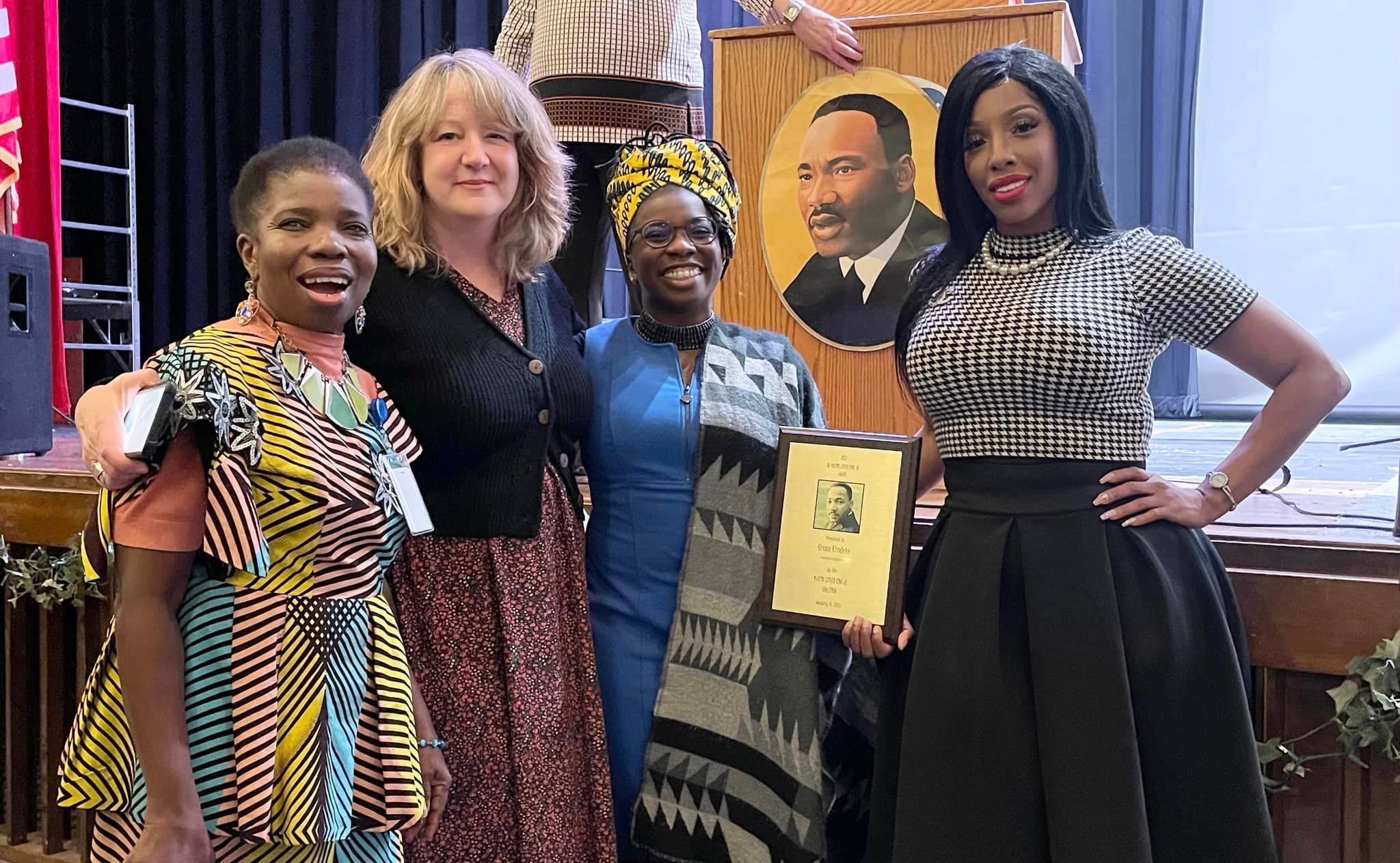 4 people standing side by side, one holds a plaque