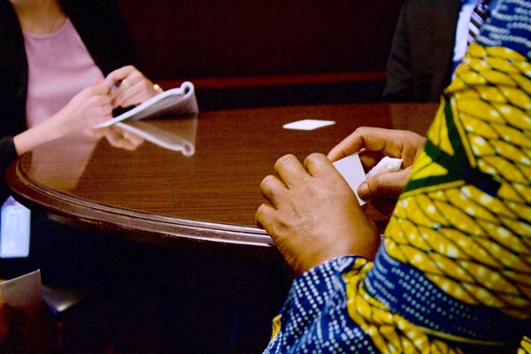 Two people's hands across a formal wood conference table, one in a suit and the other person's sleeve showing a colorful African print
