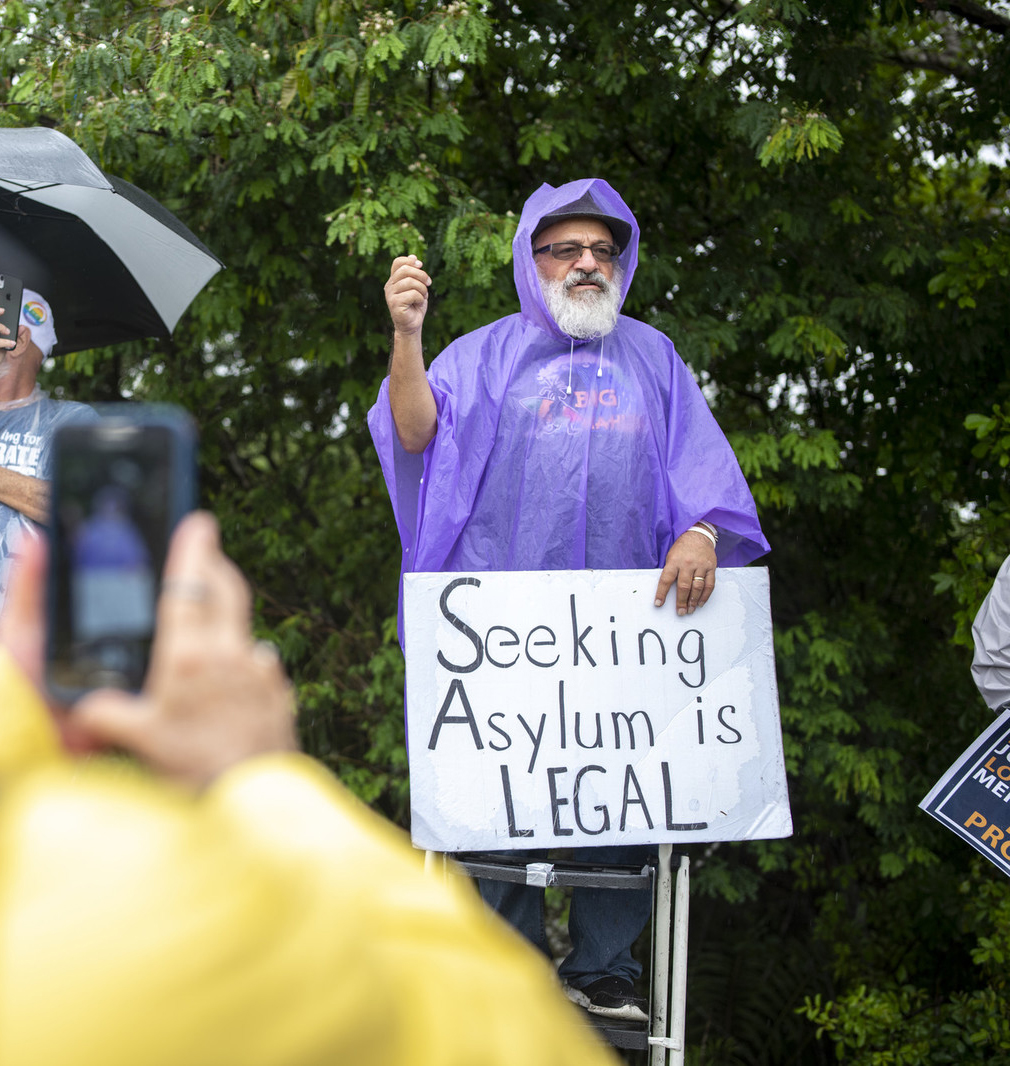 person wearing poncho holding sign that says seeking asylum is legal