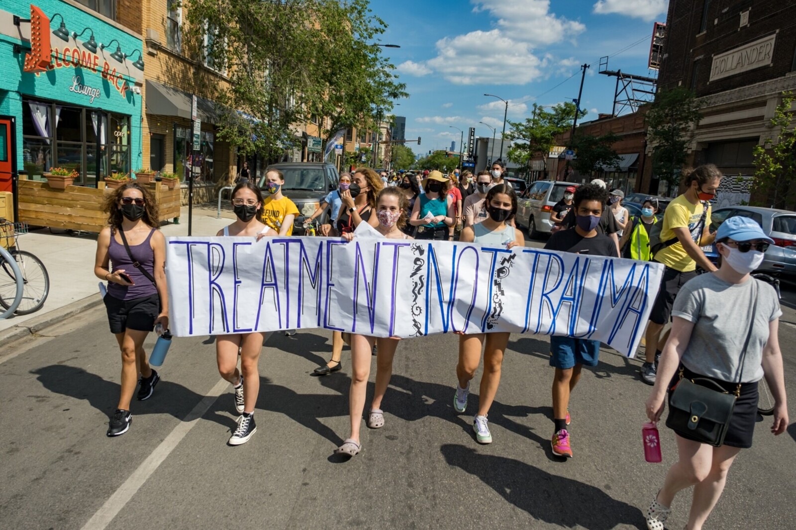 people marching down the street holding a banner that says treatment not trauma