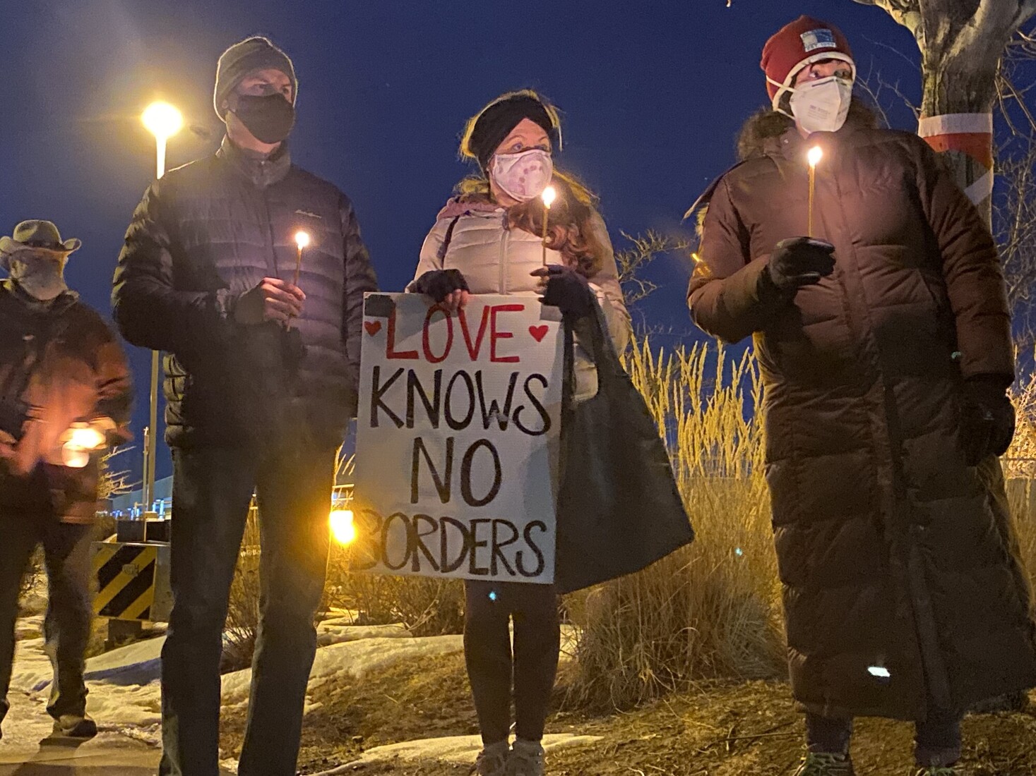 A group of people stand together, each holding candles. One person holds a sign that reads 