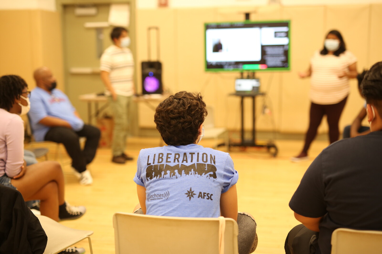 youth in a rec center listening to a presenter speak next to a virtual blackboard