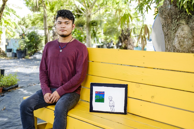 Photo of Javier Gamez sitting on a bench with their art piece