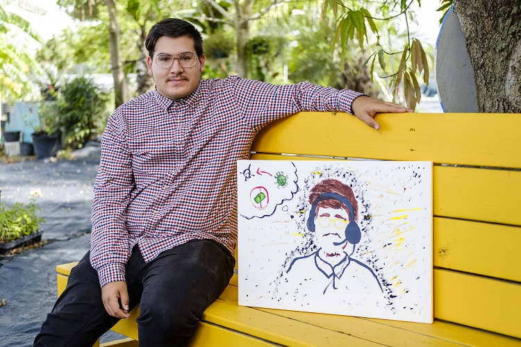 Photo of Javier Gamino sitting on a bench with their art piece