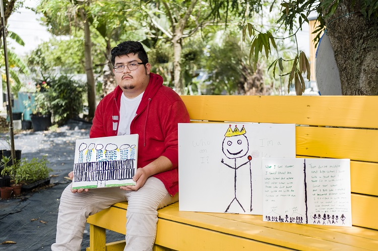 Photo of Jose Dehorta sitting on a bench with three of their art pieces