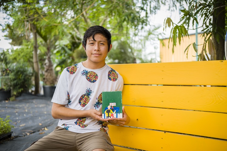 Picture of Leandro Ramirez sitting on a bench and holding their artwork