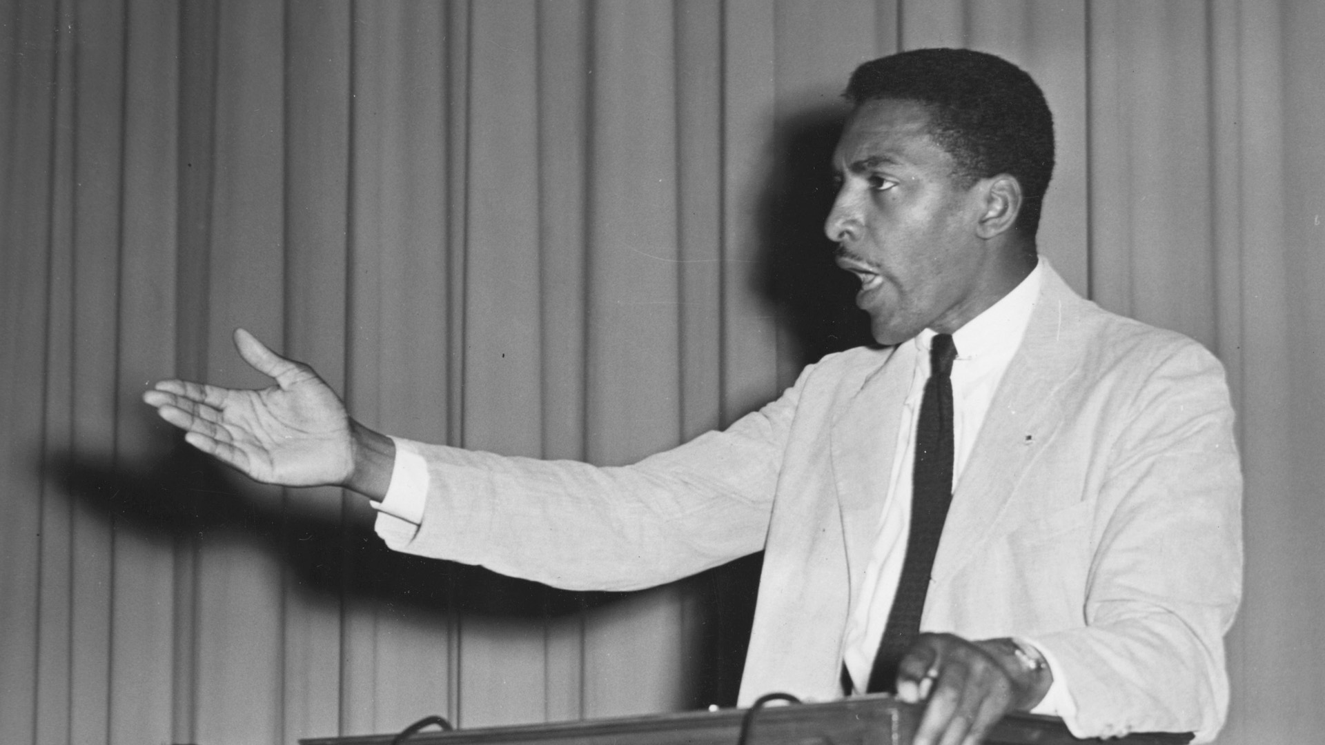 Bayard Rustin speaking at a podium with arm outstretched