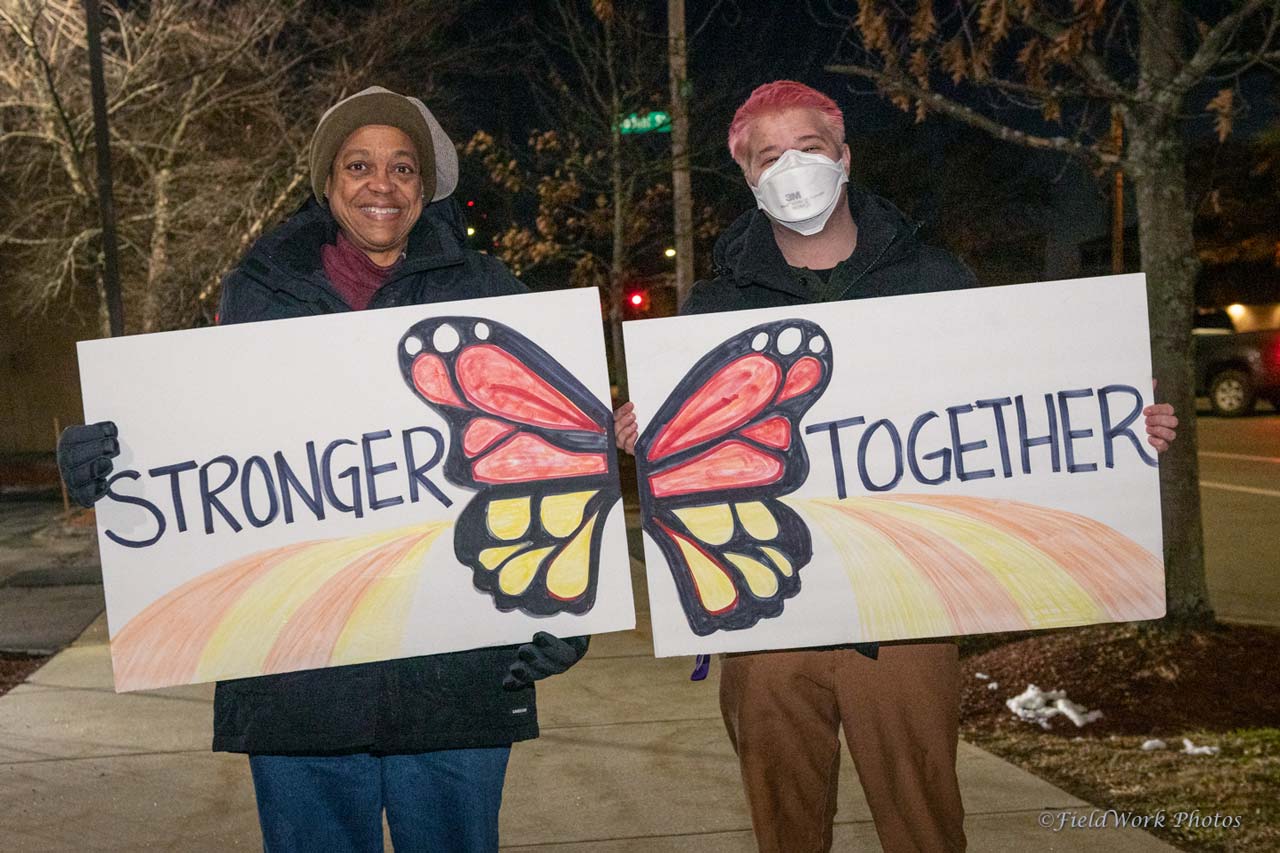 Two people holding signs that say stronger and together
