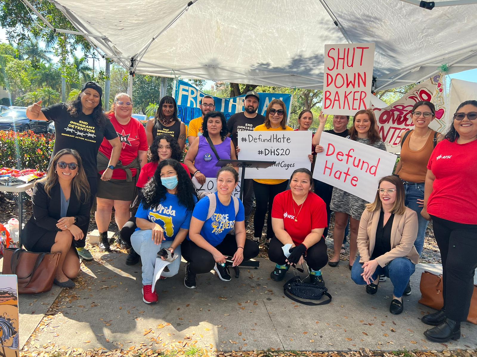 Group of people outside under a tent holding signs