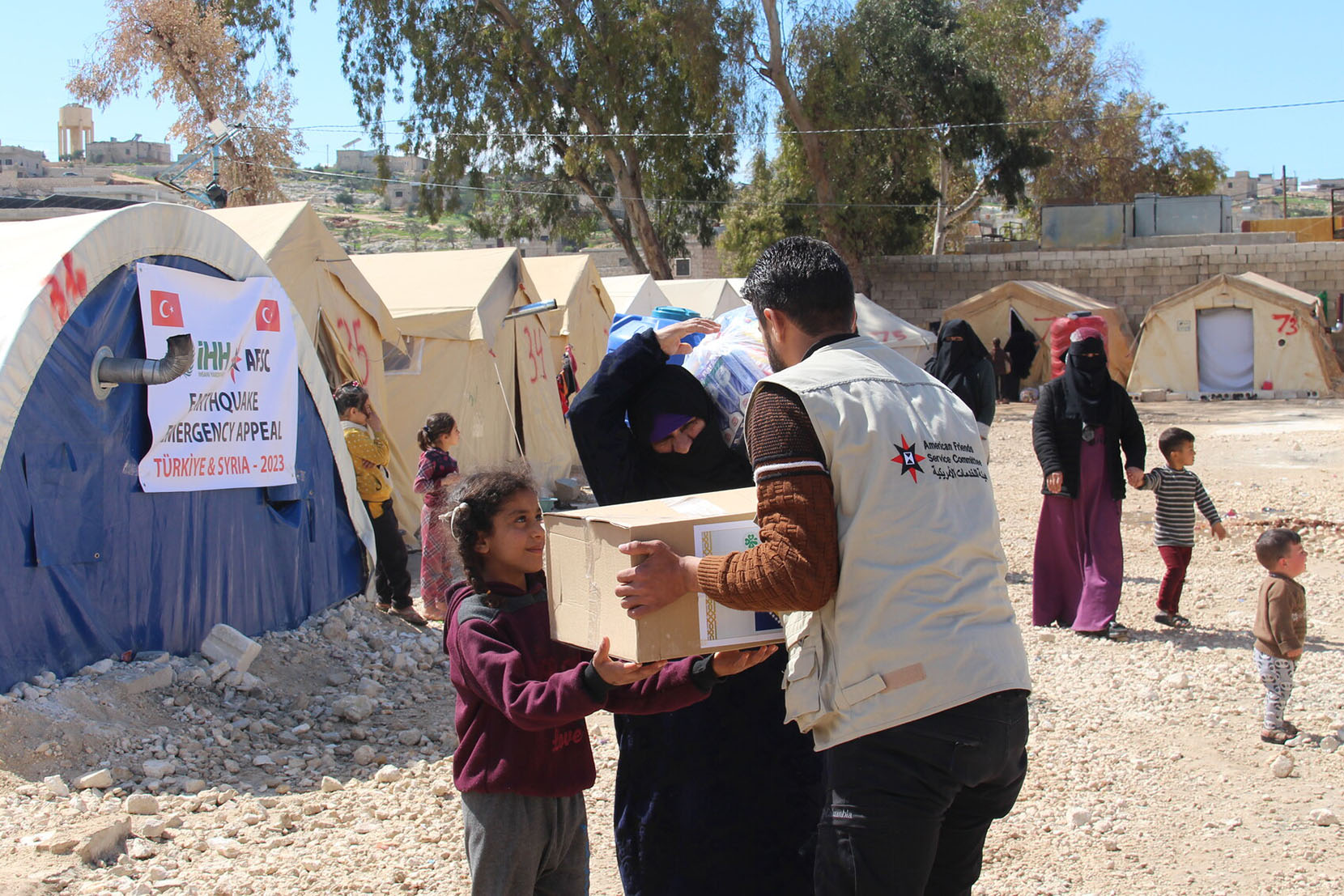 Man handing a box of supplies to a child and her guardian at a refugee camp