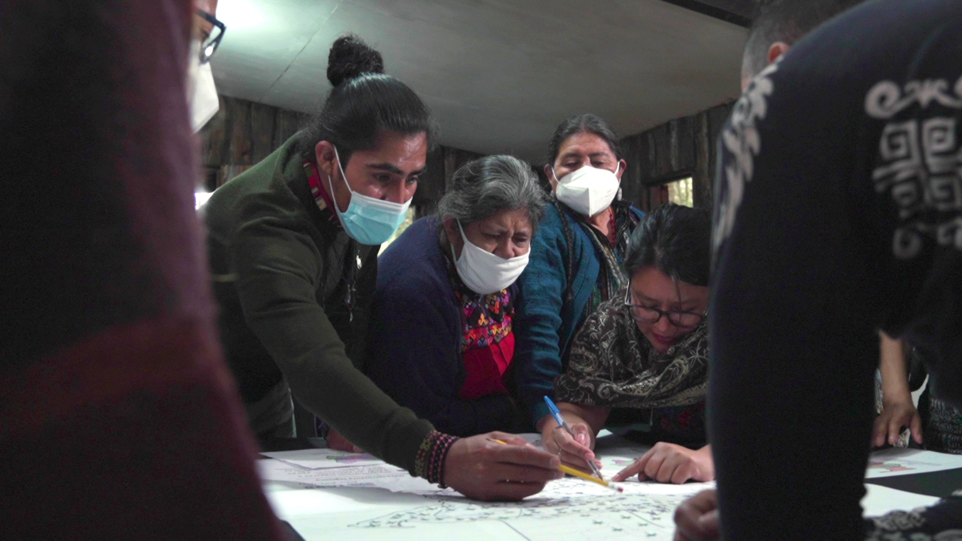 Four masked people leaning over a large sheet of paper