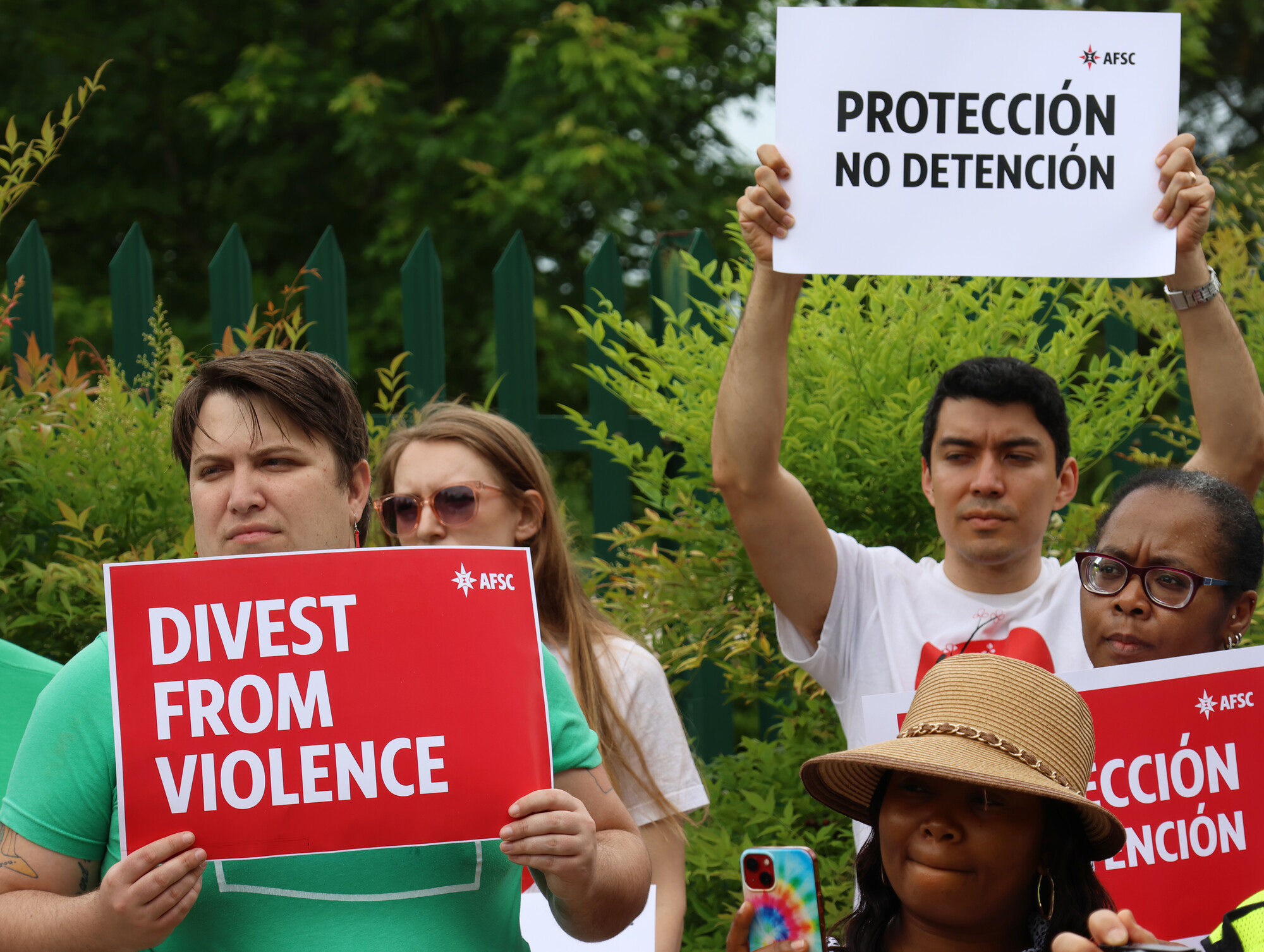 Protesters holding signs that say 'Divest from violence' and 'Proteccion no detencion'