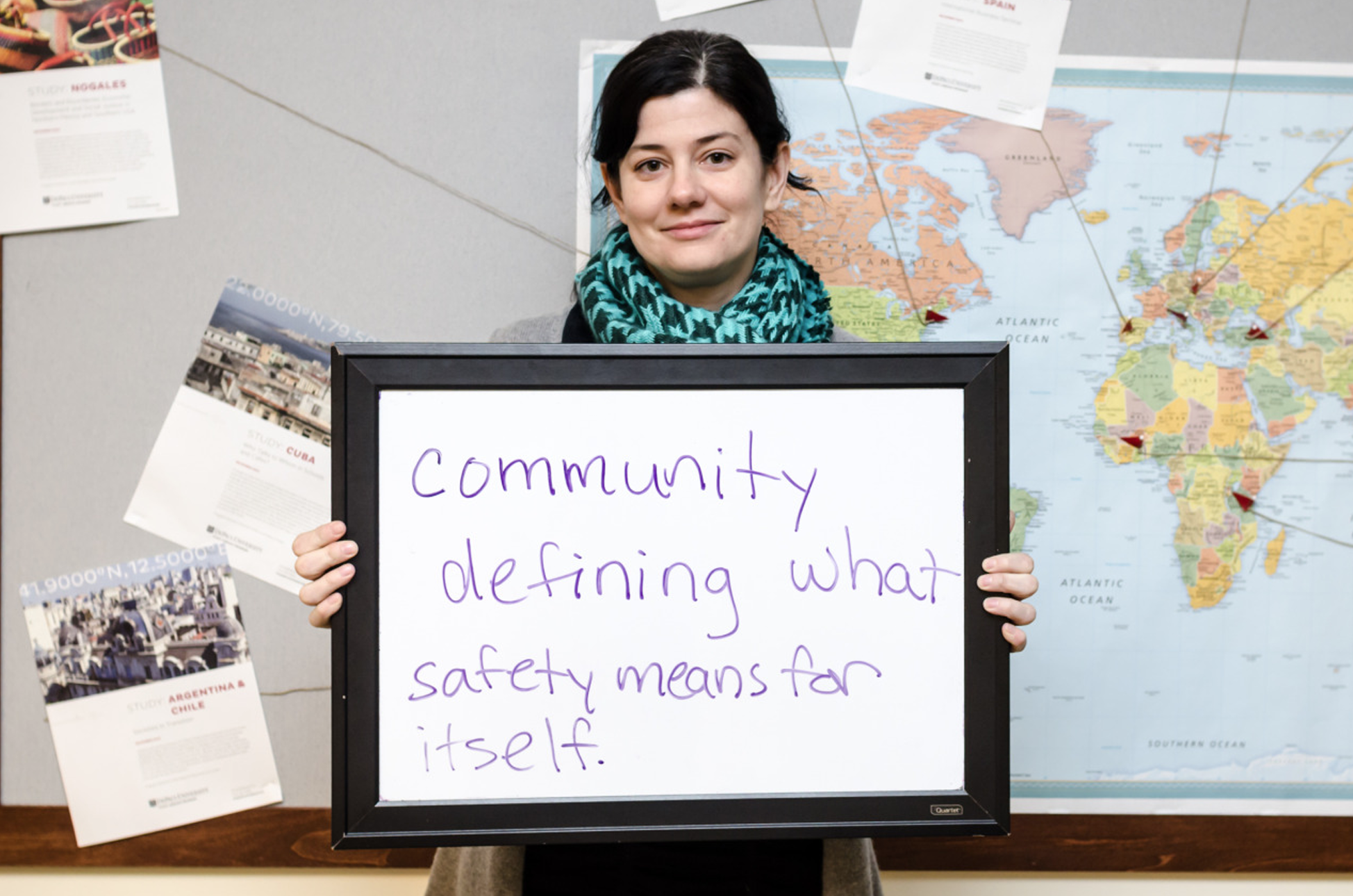 person in front of a world map holding a sign that reads community defining what safety means for itself