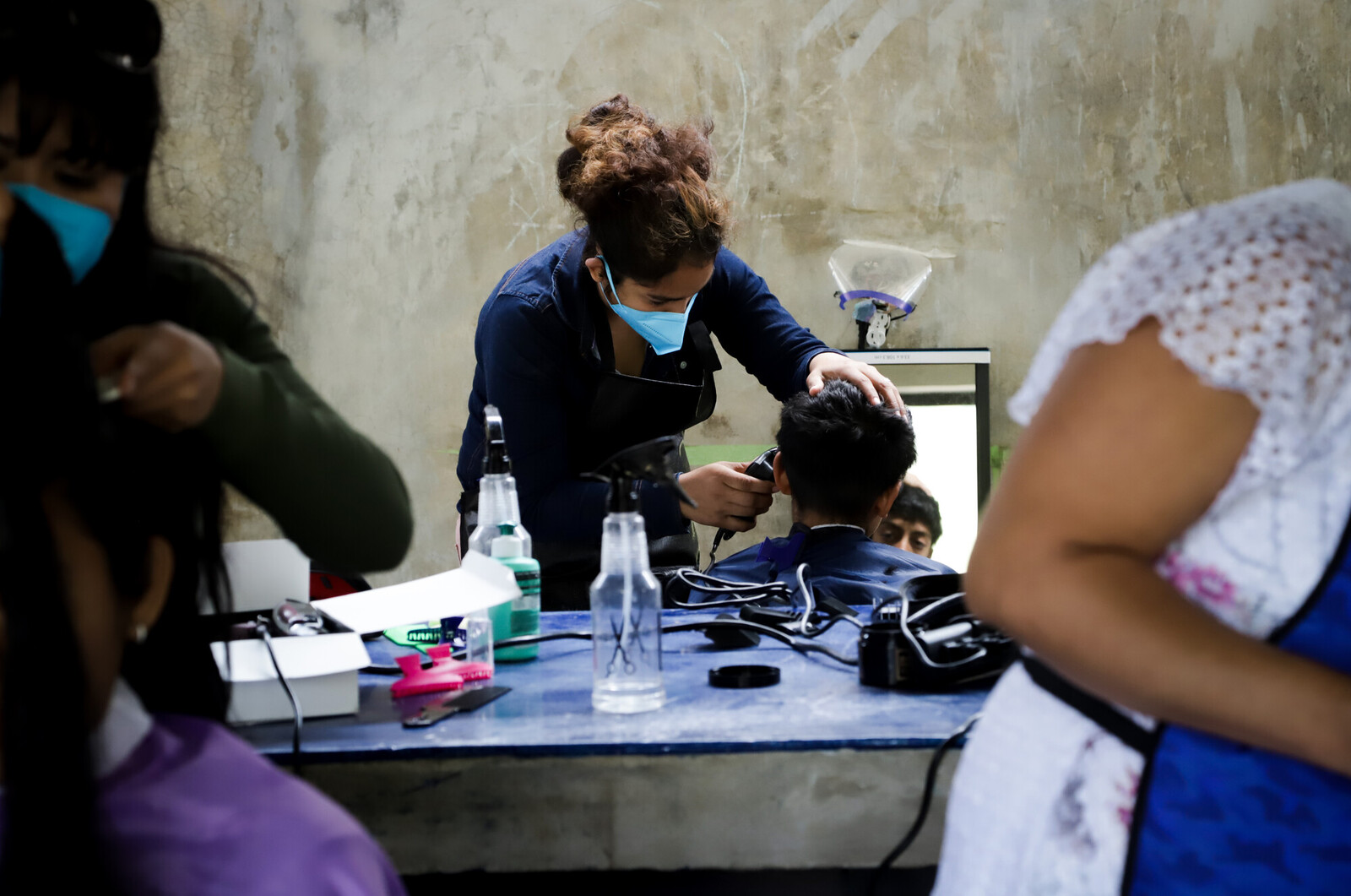 a person with a face mask cutting a childs hair in a salon