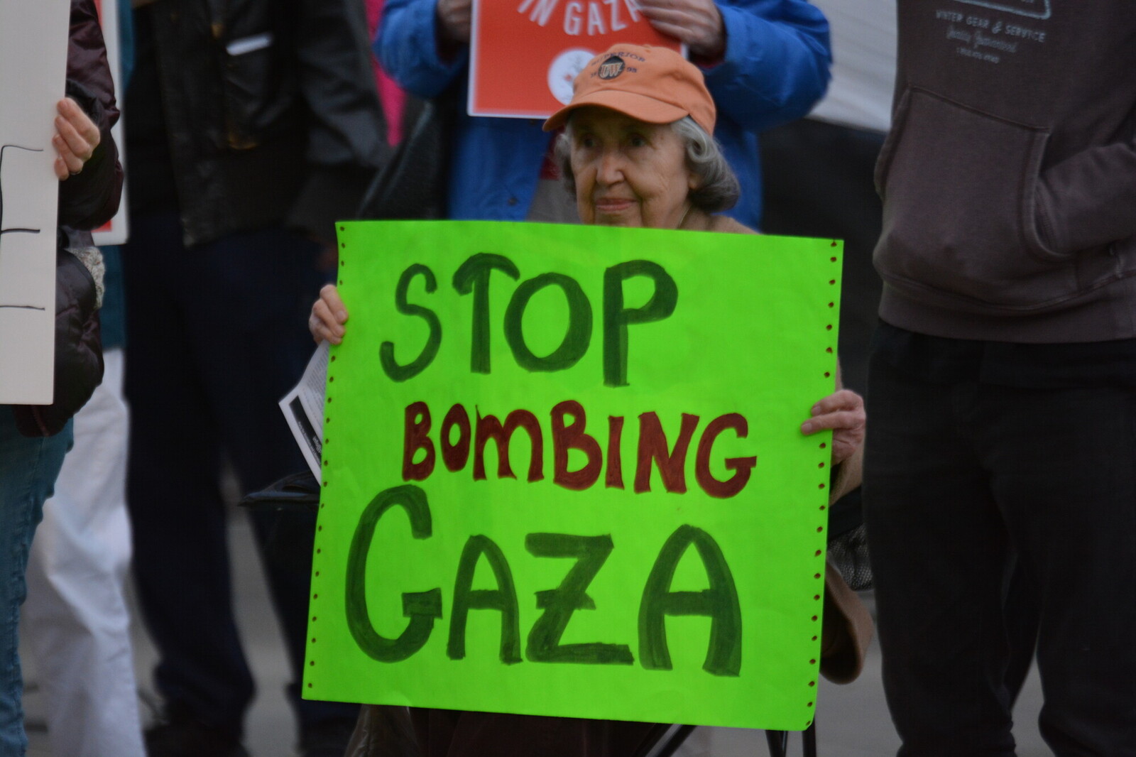 a woman wearing a ball cap holding a sign that says stop bombing Gaza
