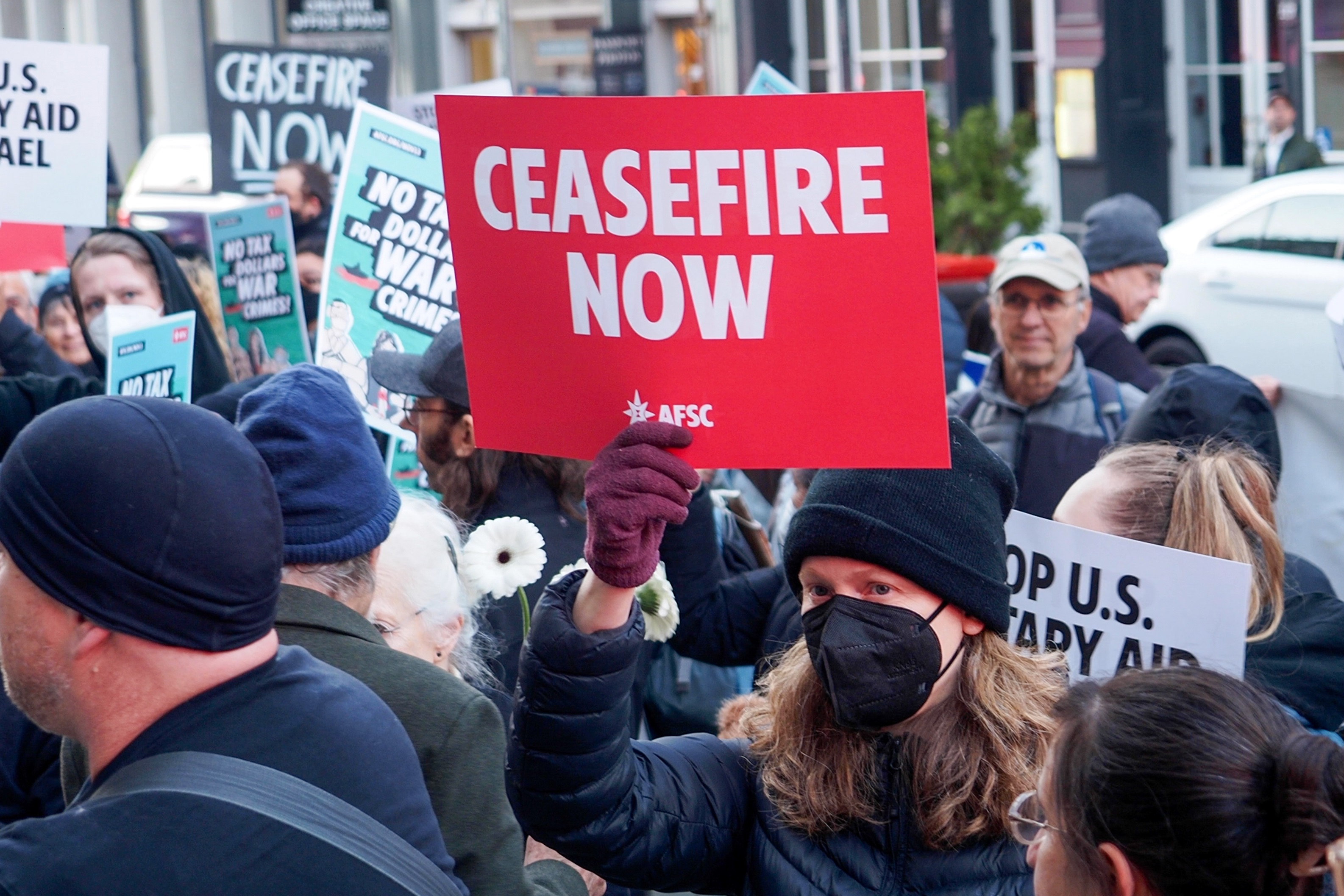 Person in face mask holds red ceasefire now sign