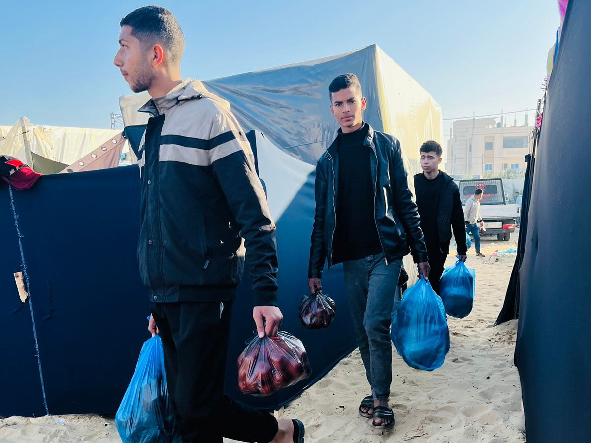 3 men carries plastic bags of food between tents