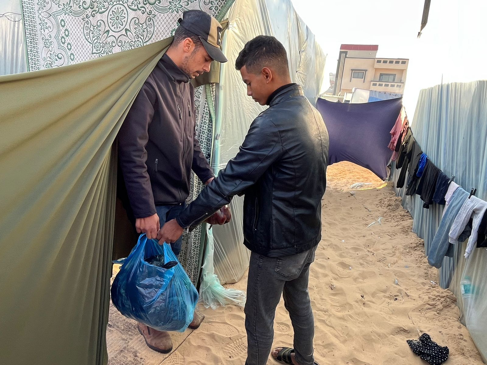 Man hangs bag of food to another man in a tent
