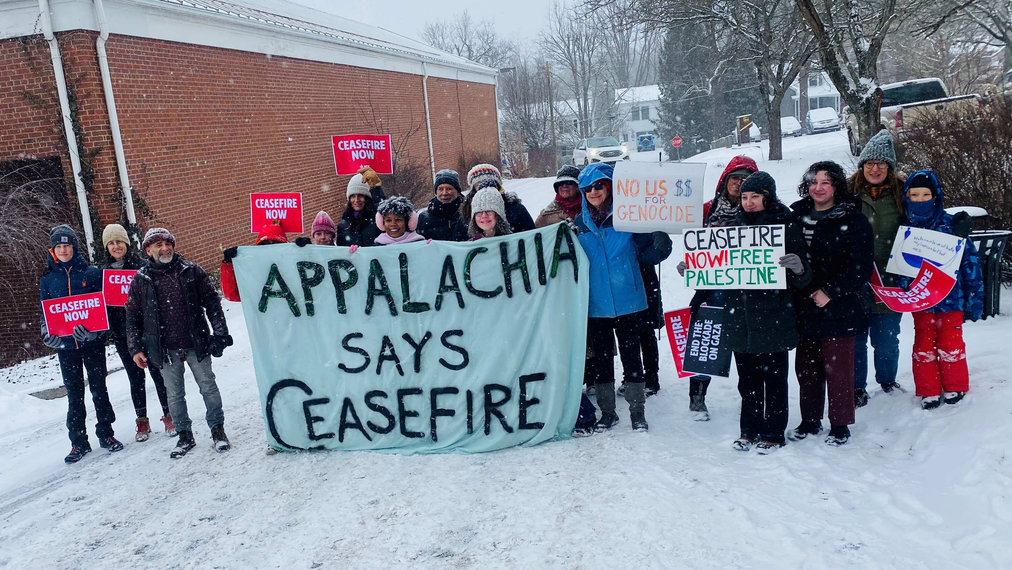 People in the snow with a painted banner that reads 'Appalachia Says Ceasefire'