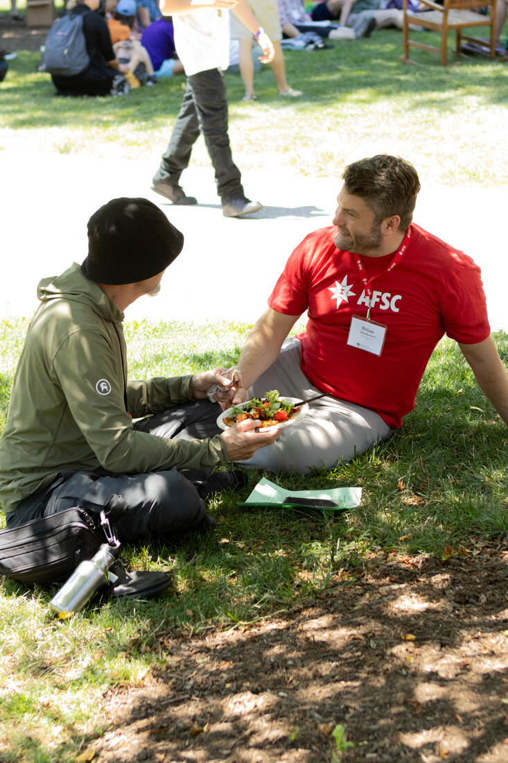 AFSC staff member and Friend sit in the grass under a tree