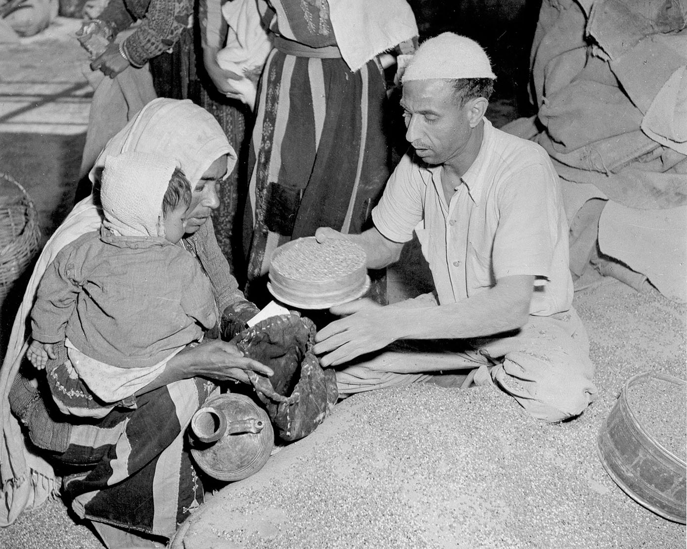 A person offering a container of grains to a woman and child.