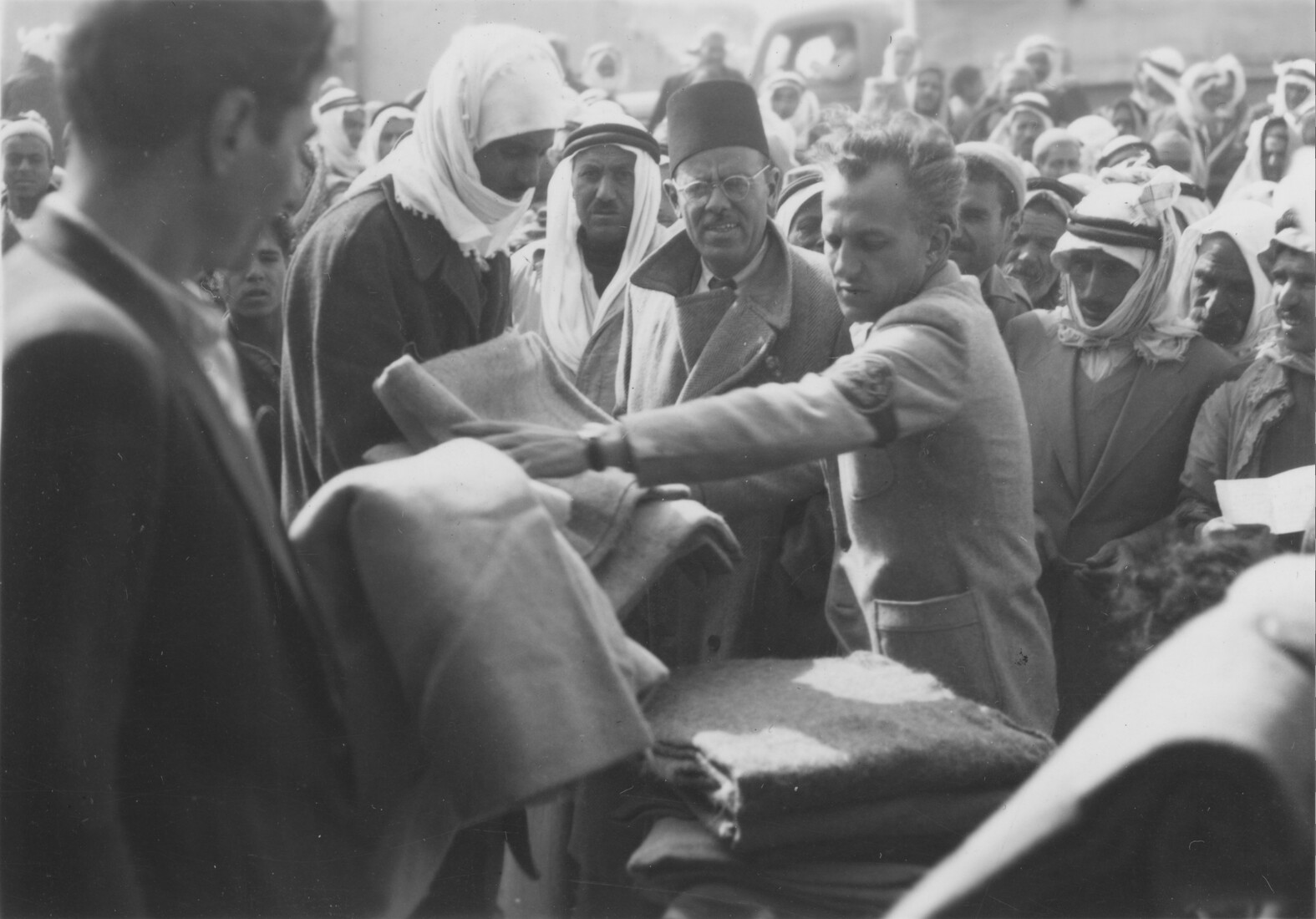 Archival photo of a person distributing blankets in a crowd