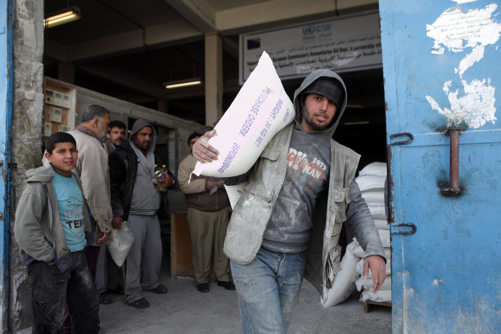 A man carrying a large sack on his shoulders exits a factory