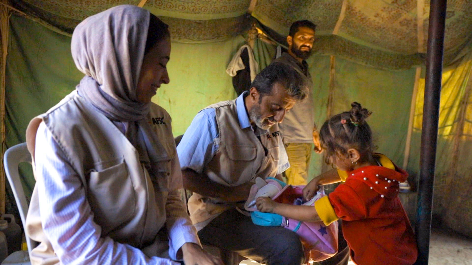 Two AFSC staff members sit inside a tent in Gaza distributing school supplies to children