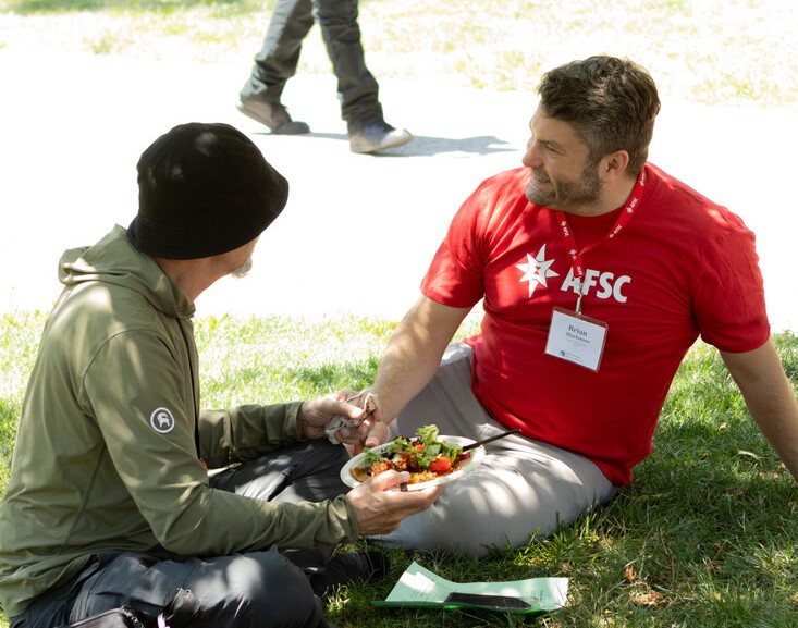 AFSC staff member and Friend sit in the grass under a tree