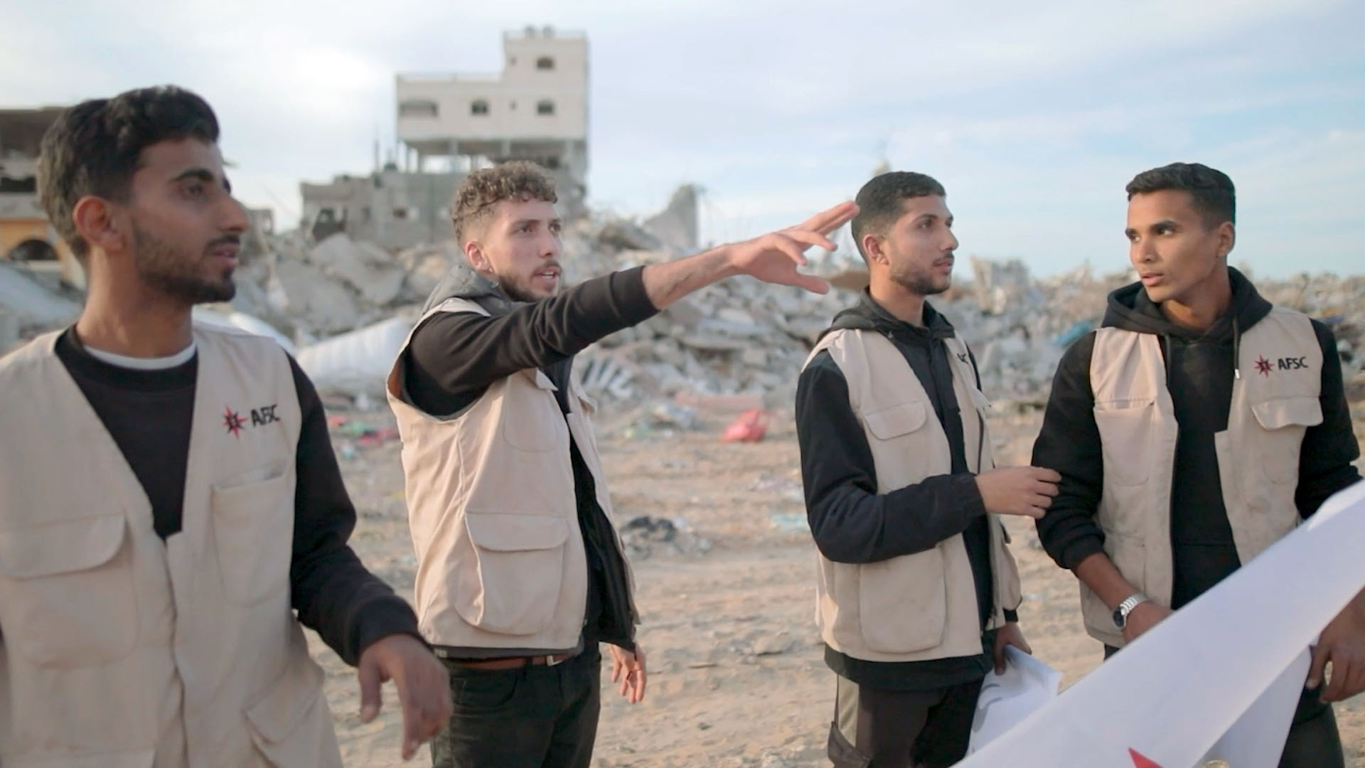 Four people stand outside surrounded by rubble