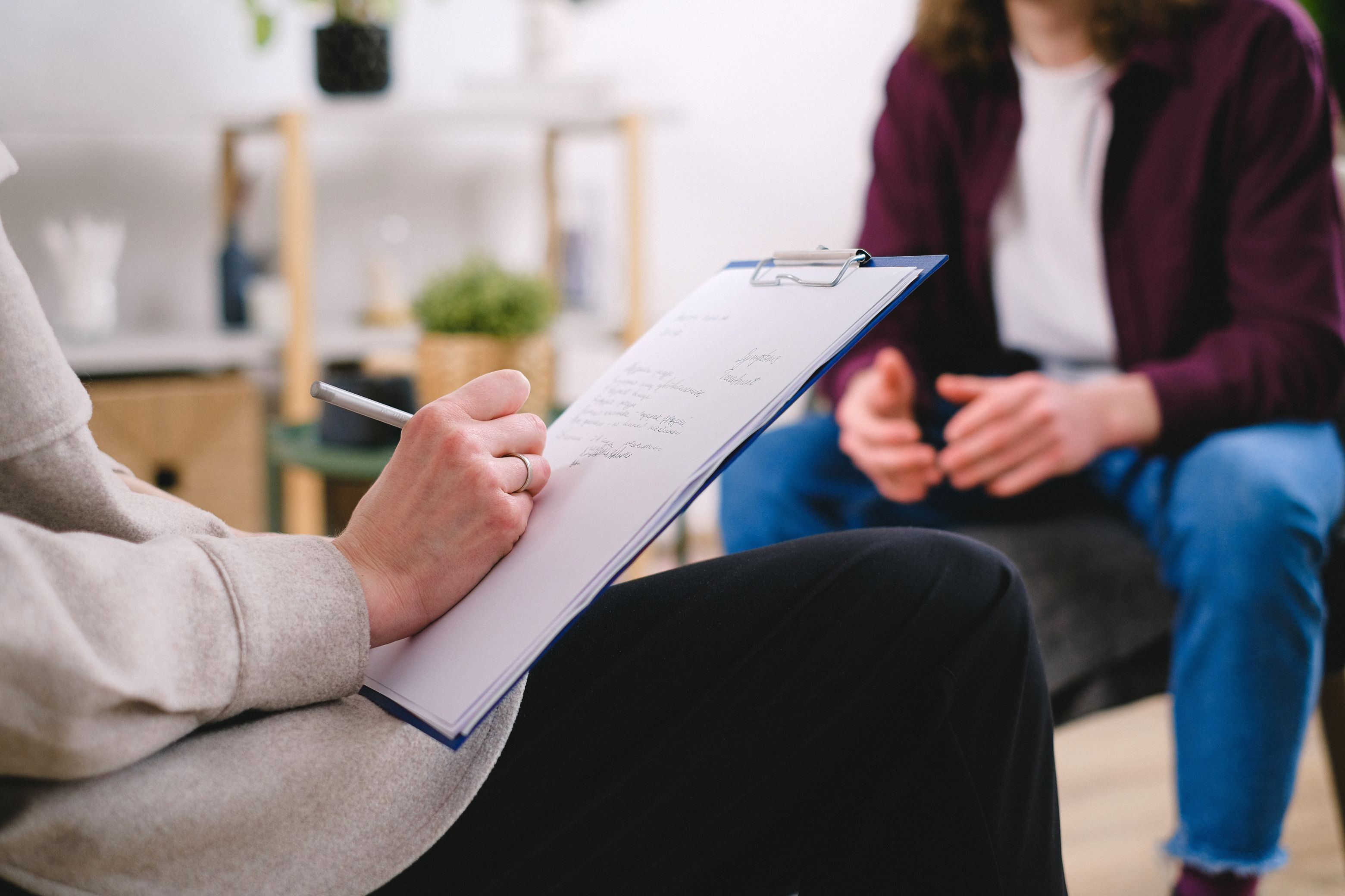Image of a person taking notes on a clipboard while listening to another person
