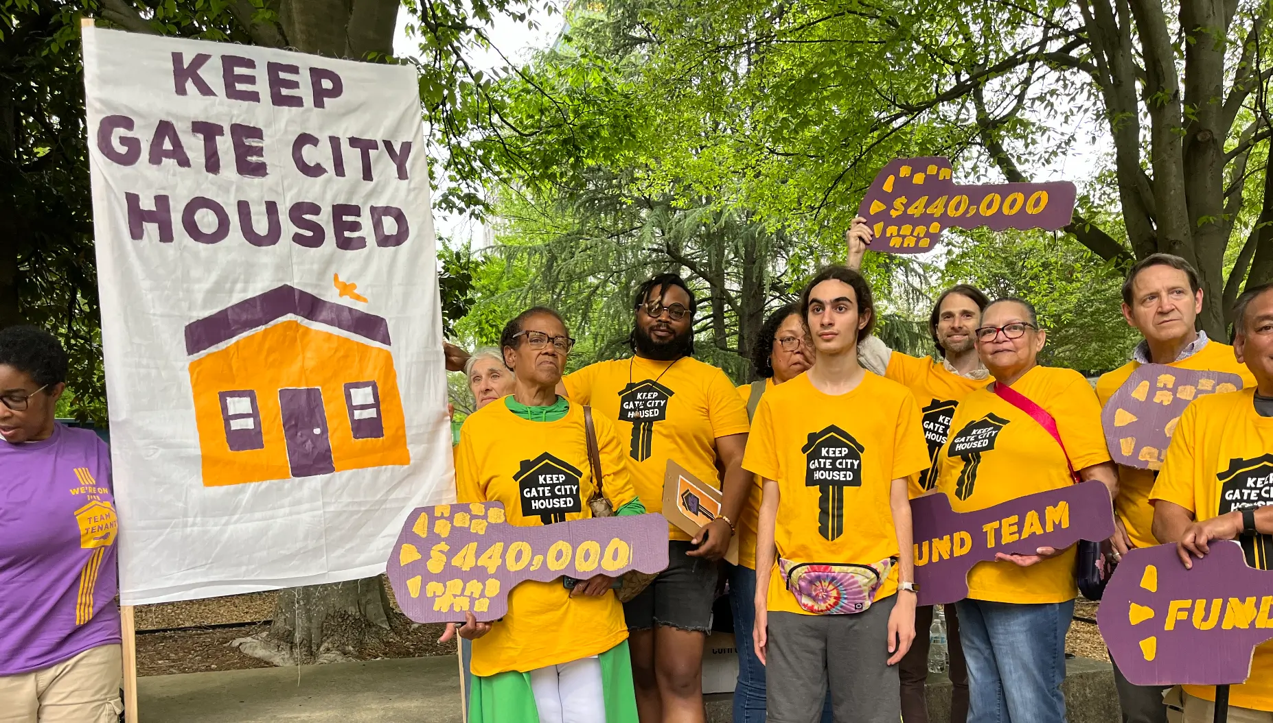Image of a group of people in yellow shirts with signs that say 'Keep Gate City Housed'