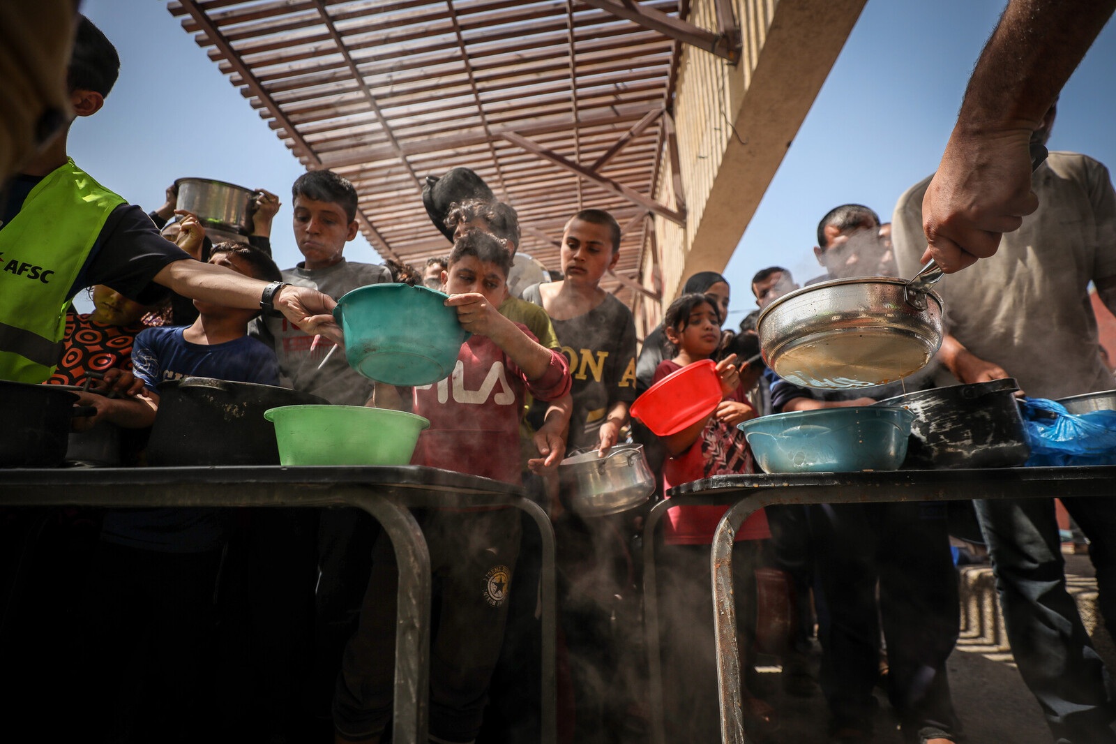A hot meal is distributed to children holding pots in Gaza