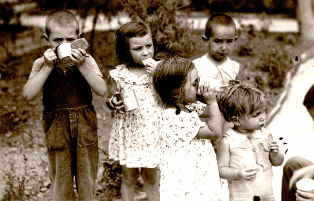 Black and white photo of children drinking from metal tins