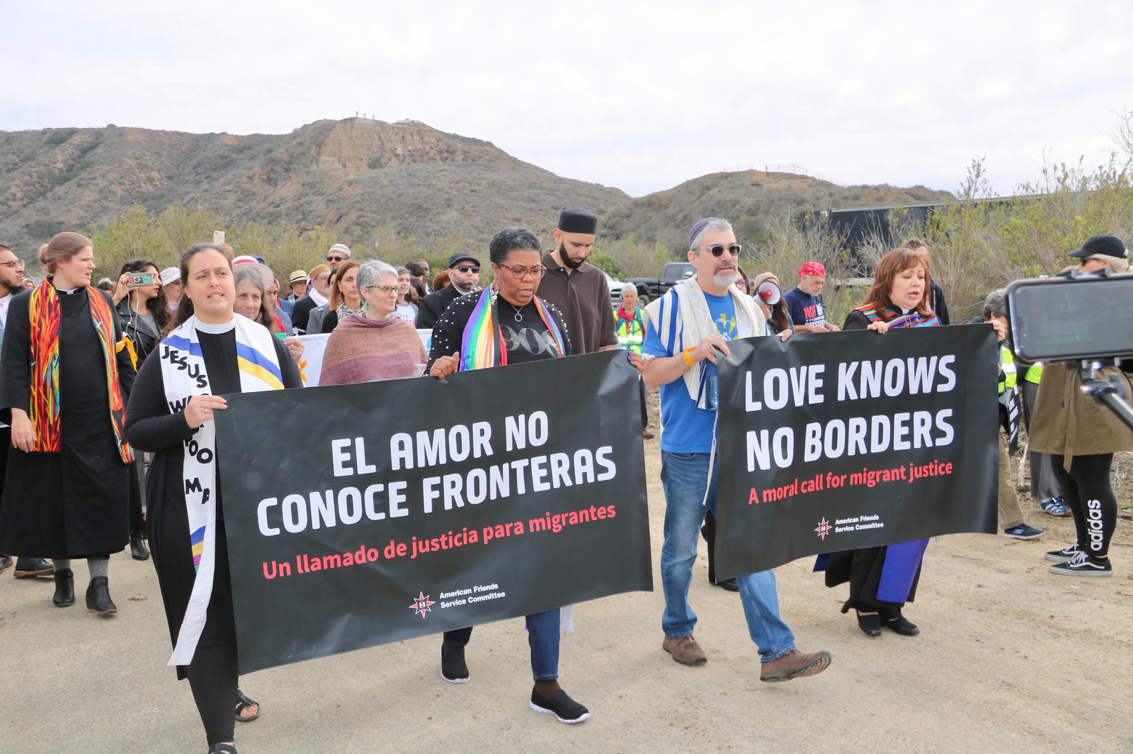 People march down a dirt road holding two large banners