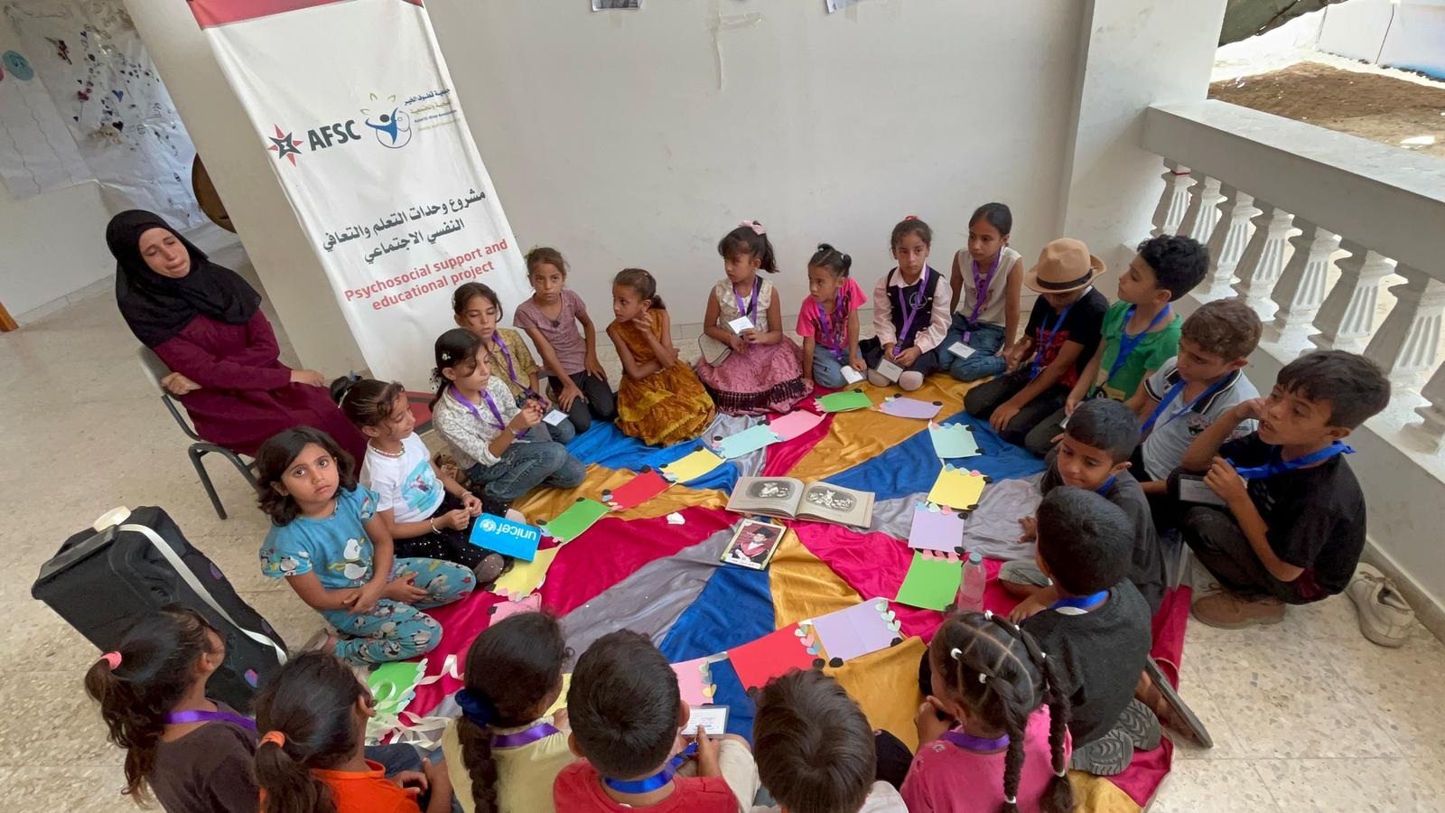 Woman sits in chair as children sit on a circle on the ground.