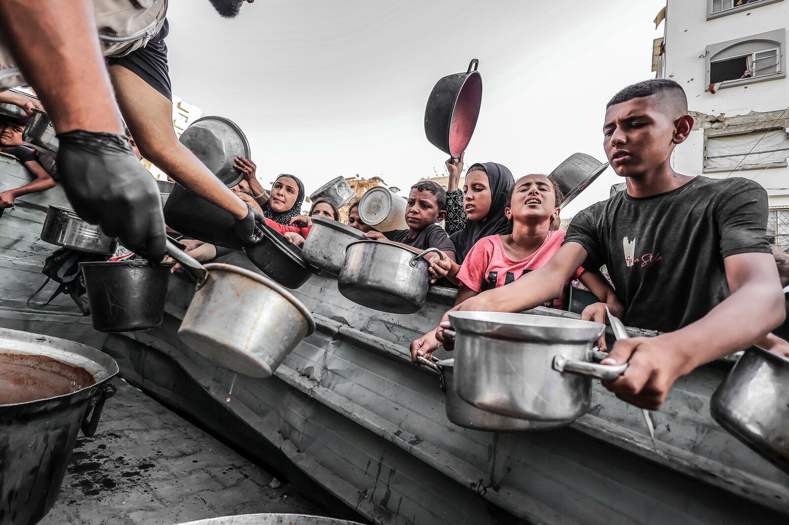 A row of children hold out pots waiting for oup