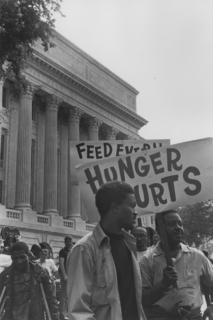 Two men protesting outside a federal building, with a sign reading 'Hunger hurts.'