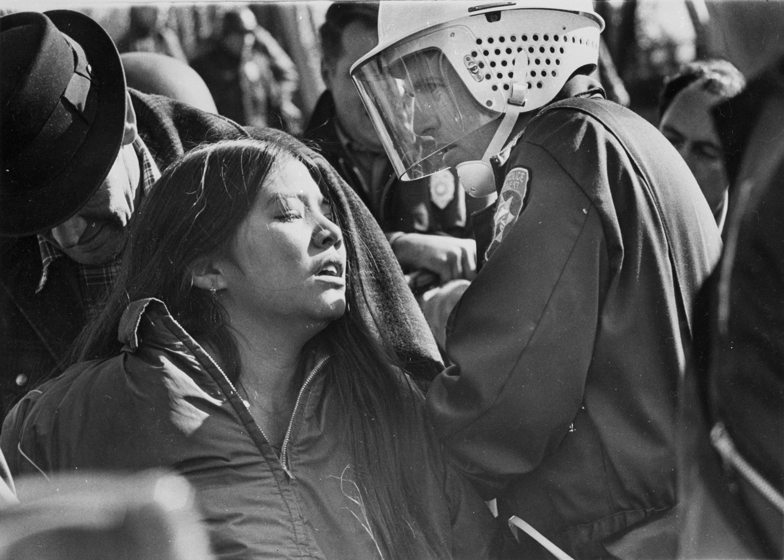 Woman in a dense crowd being arrested.
