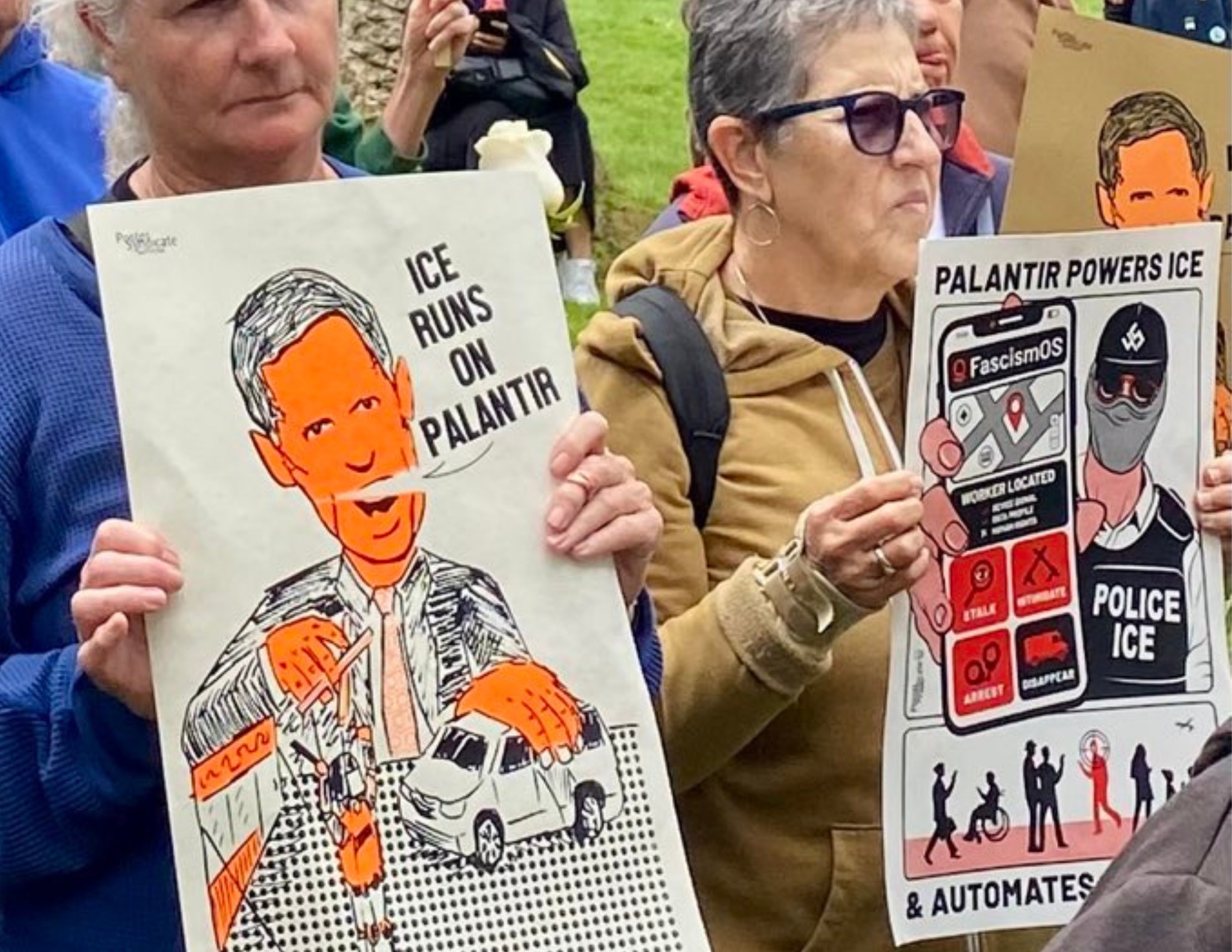Two women holding signs at a protest. One reads: 