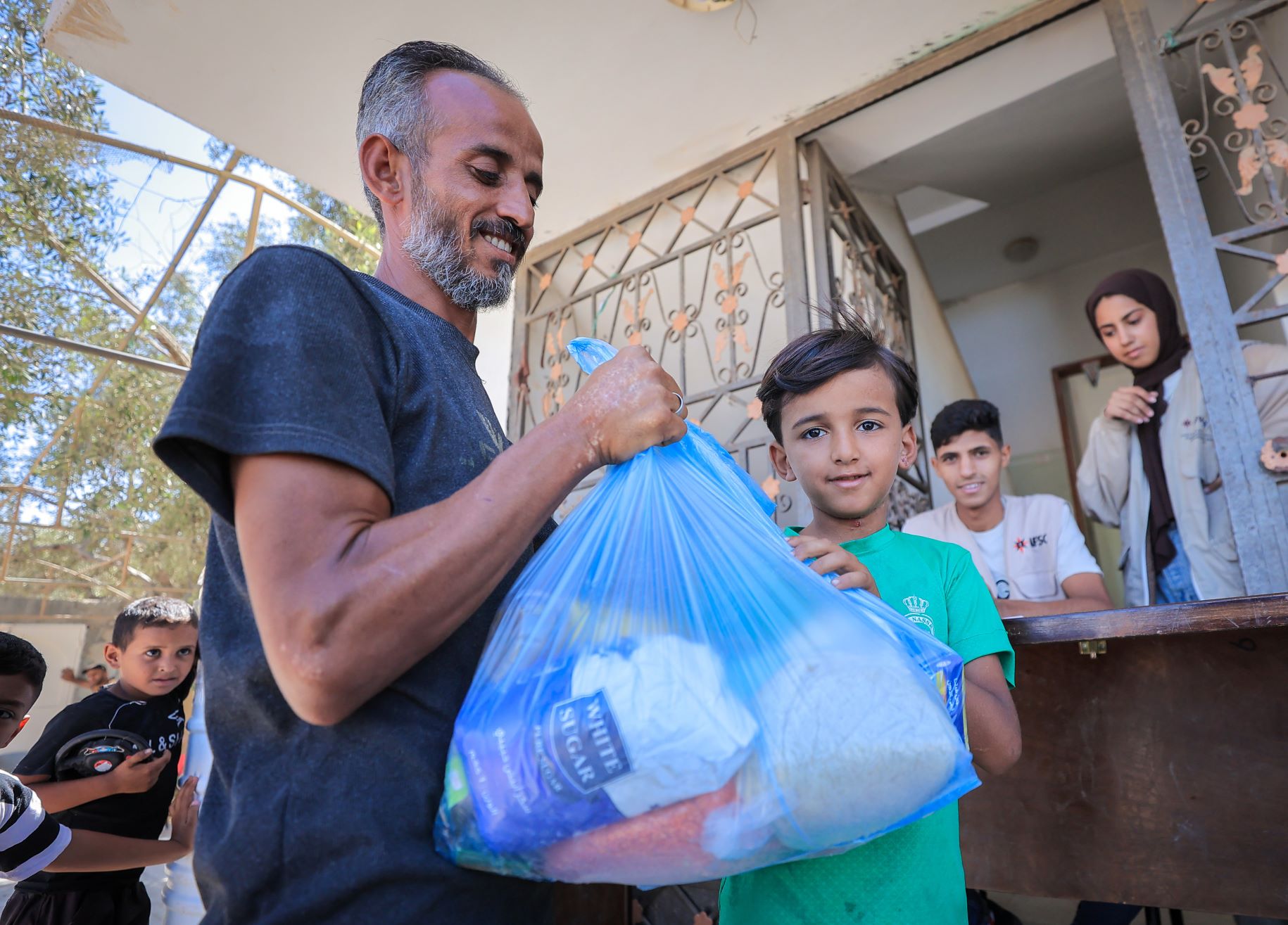 A smiling adult holding a bag of supplies beside a child in Gaza