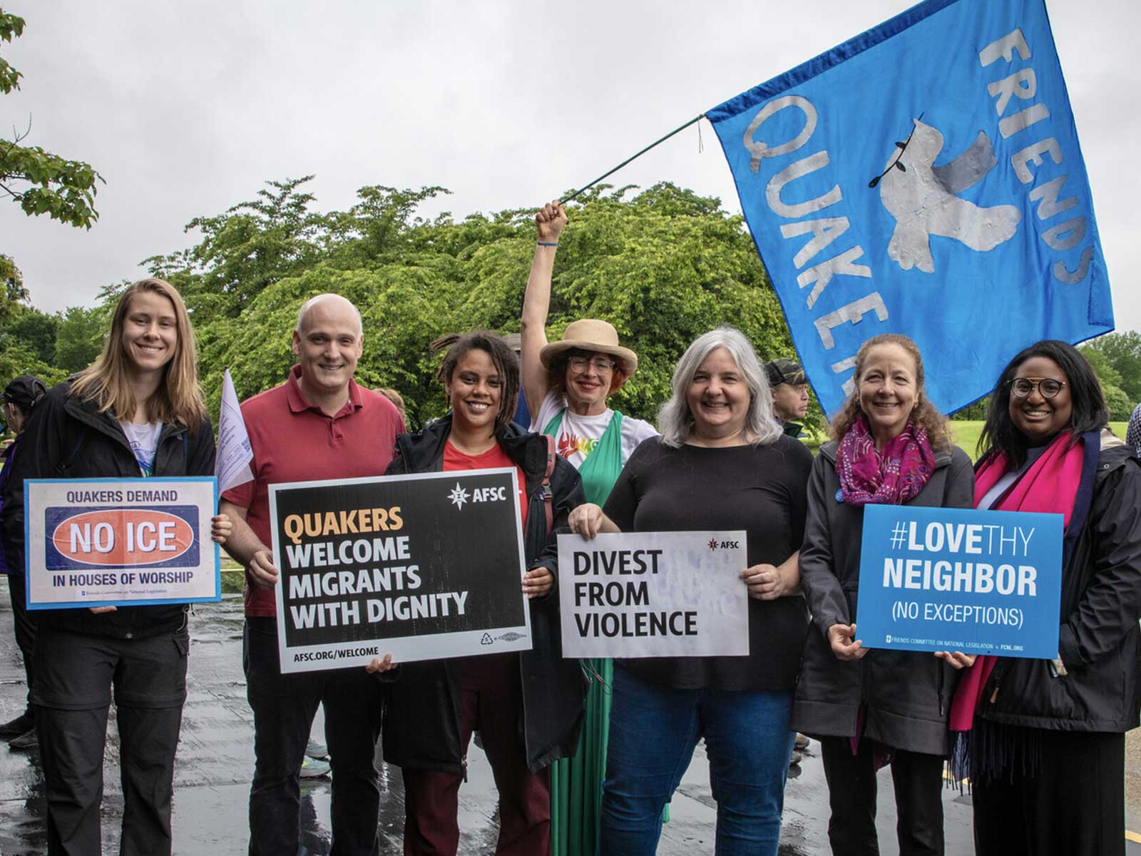 a group of six people holding up quaker protest signs. Some signs read, divest from violence. another says 