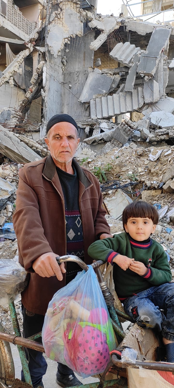 A man and child with rubble of a building behind them